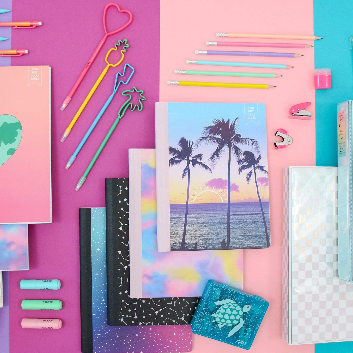lifestyle image of palm tree, tie-dye, celestial and space galaxy composition books shown with other school supplies
