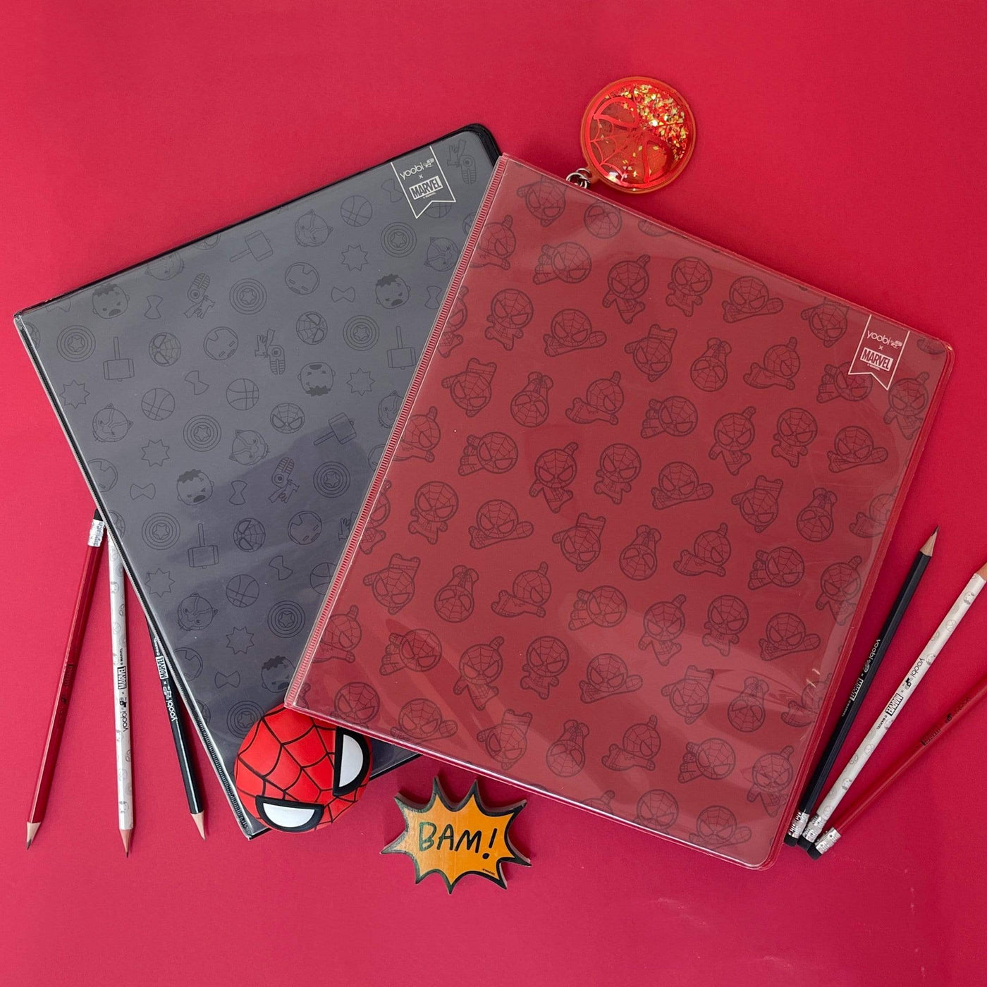 lifestyle image of Avengers black icon binder and red Spider-Man icon binder shown with pencils and sharpener